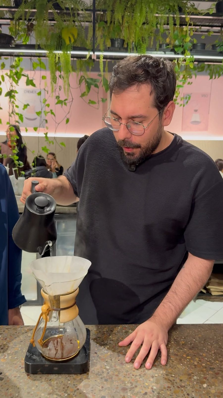 Barista de L'arôme preparando un Chemex entre plantas
